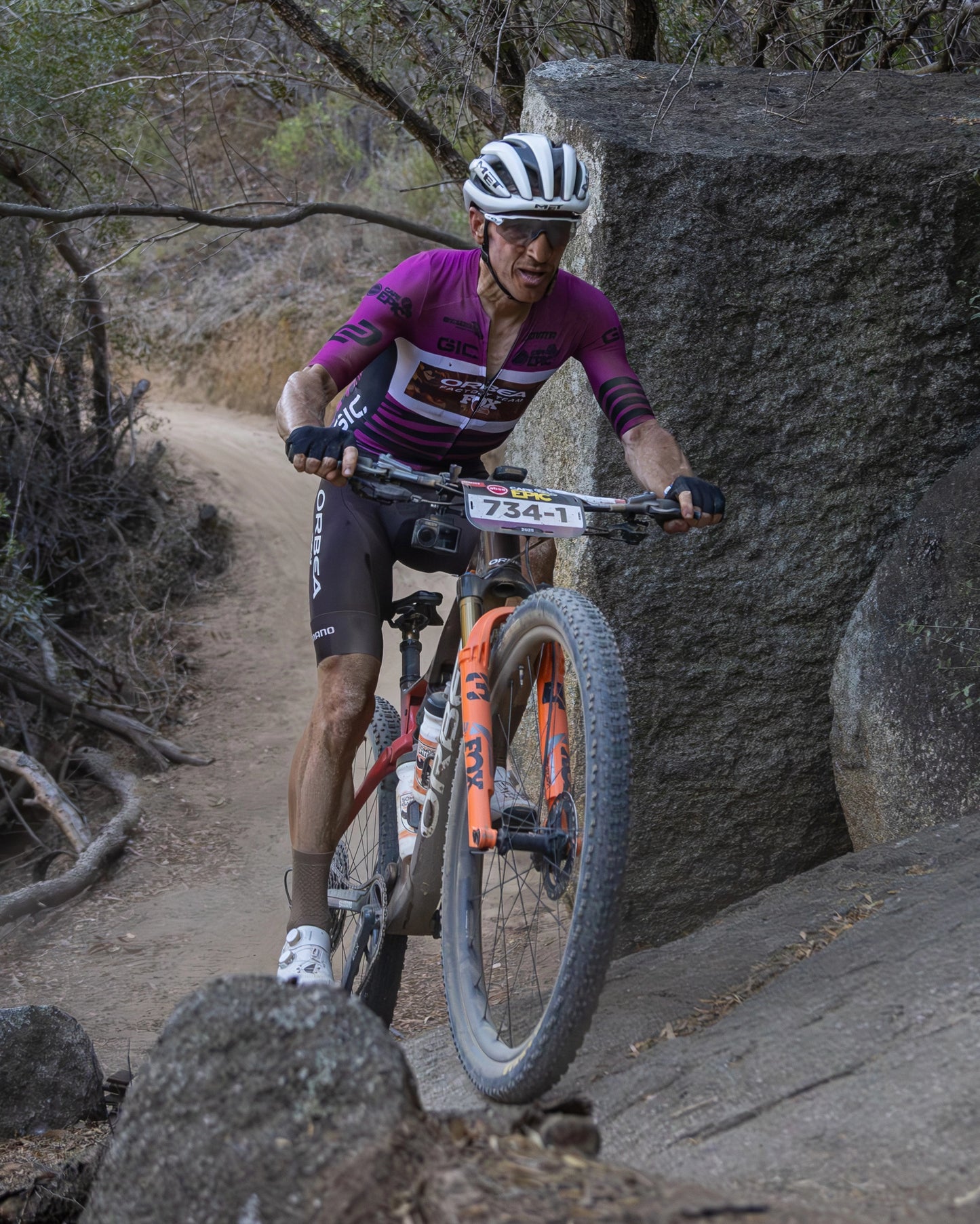 Ciclista con maillot oscuro bajando una curva cerrada en un sendero de tierra suelta y piedras, mostrando control técnico y postura agresiva sobre la bici de gravel con neumáticos gruesos