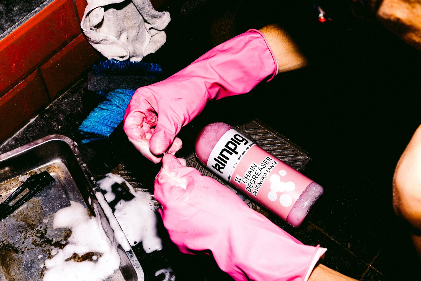 manos con guantes rosas sacando desengrasante rosa para las bicis,