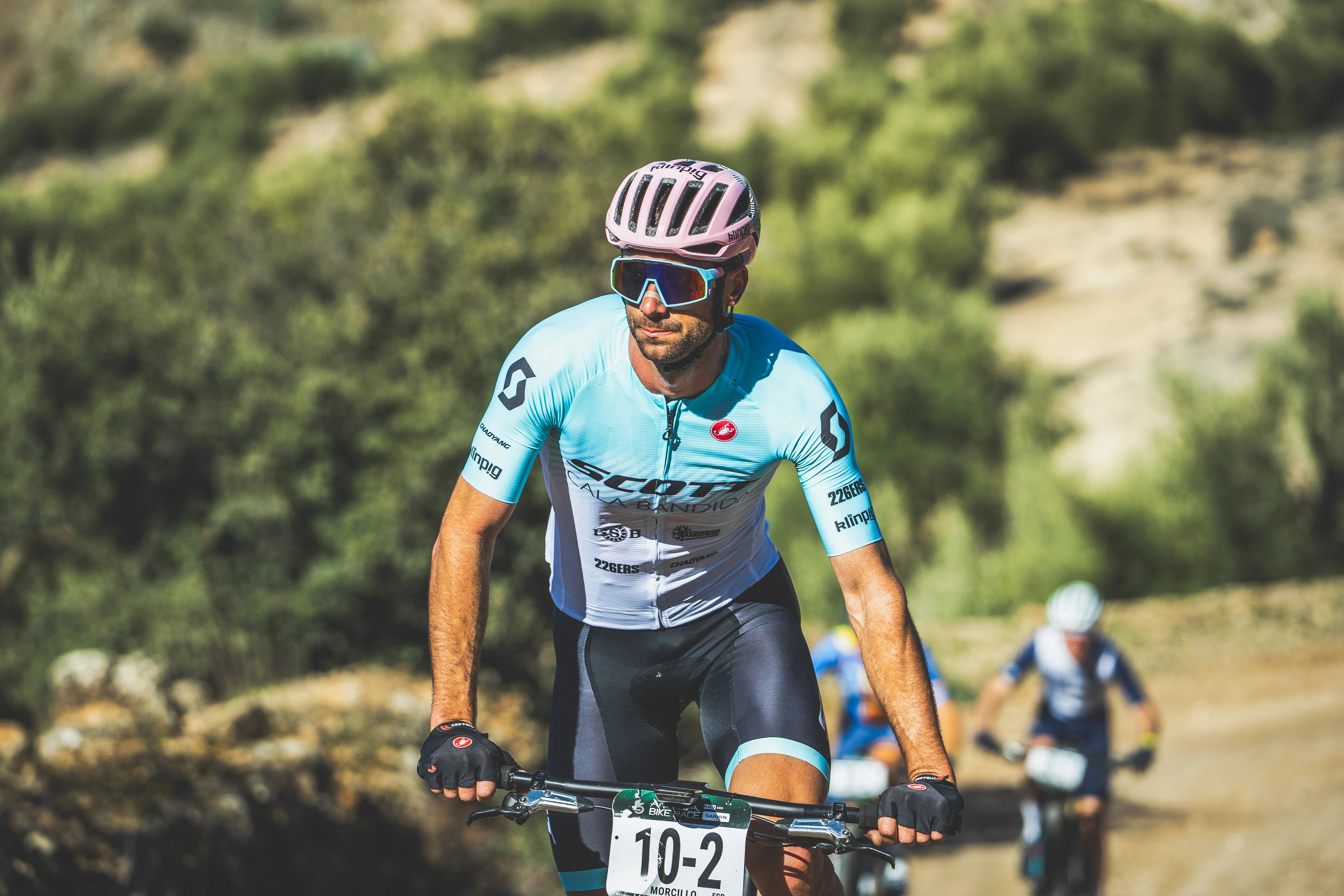 fondo de arbusto corredor de gravel con maillot azul y blanco casco rosa corredores atrás