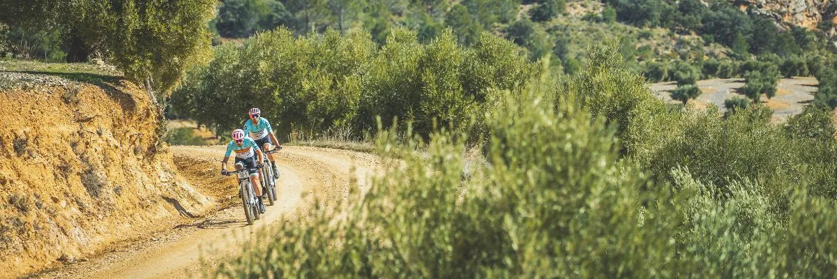 camino de tierra corredores de bici con casco rosa ruta con arbustos 