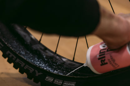 camra de bicieta envase blanco con etiqueta rosa roceando liquido radio de bici